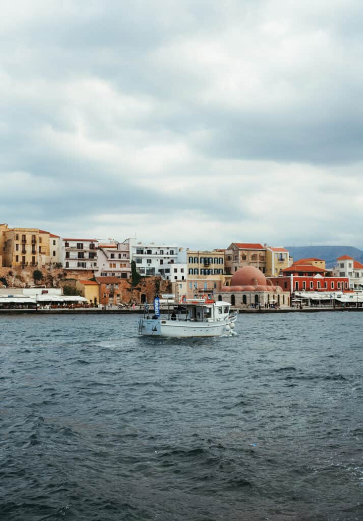 a boat sailing through the harbor in Chania, Crete. You can see beautiful Venetian buildings lining the harbor.