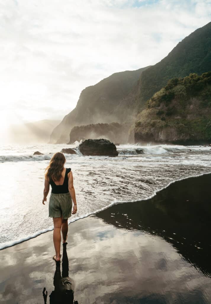 Seixal beach in the morning on a foggy day. Sarah is walking along the black sand toward the ocean. There are mountains in the background