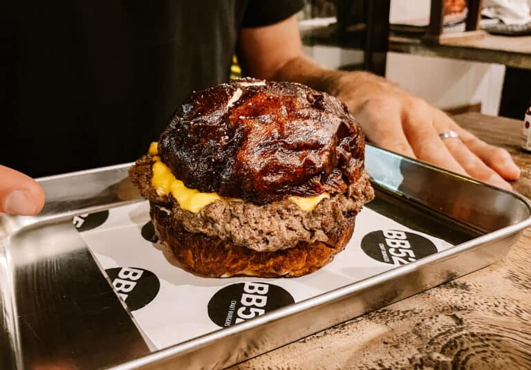 A mouthwatering gourmet burger from BB52 in Canggu presented on a metal tray, featuring beef patty with melted cheese, topped with caramelized glaze.