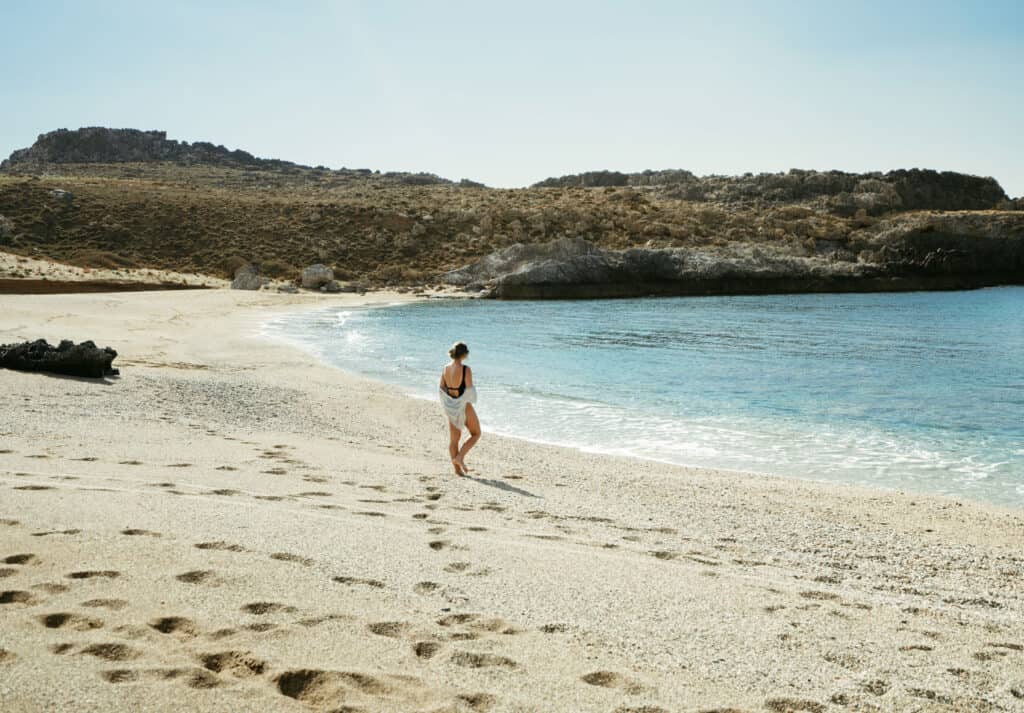 Sarah walks along the sandy shore of Skinaria Beach in Crete, leaving footprints behind her.