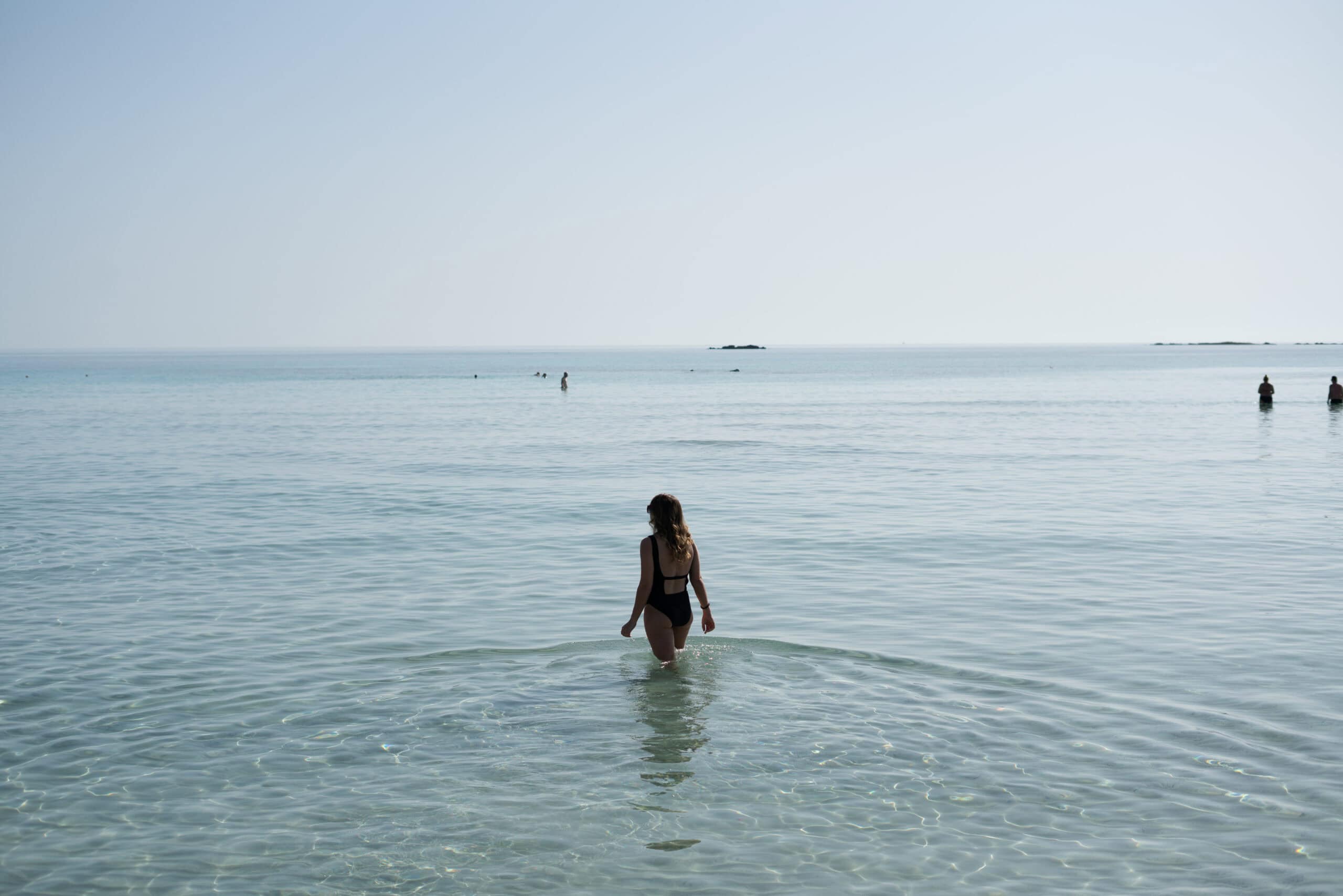 Sarah in a black swimsuit walking in the shallow bay at Elafonisi Beach