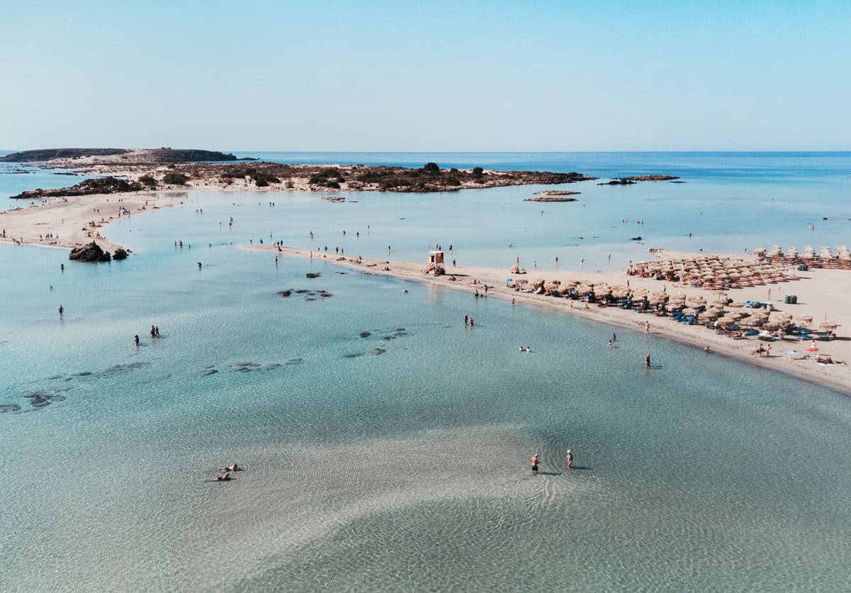 An aerial view of Elafonisi Beach looking out towards Elafonisi Island with people walking in the shallow water.