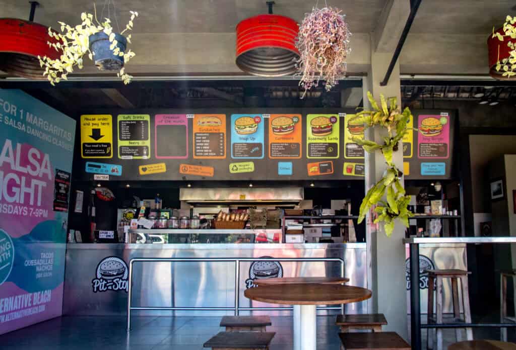 The interior of Pit Stop restaurant, featuring a colorful menu board displaying various burger options and other items like soft drinks and milkshakes.