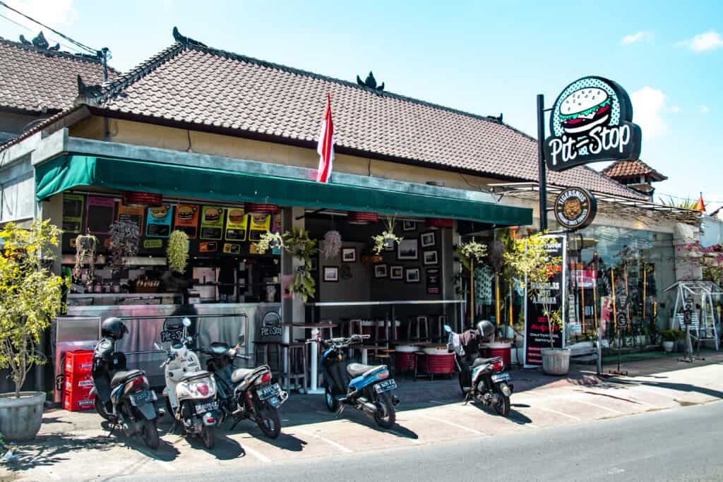 A street view of Pit Stop, a restaurant with a green awning and a sign featuring a cartoon burger.