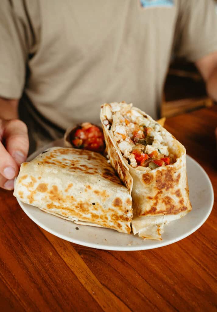 a delicious chicken and cheese burrito cut in half and served with a side of pico de gallo