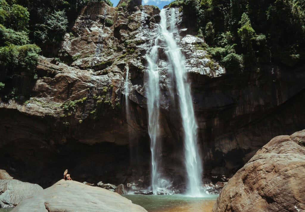 Sarah sitting high on a massive rock at the foot of Aberdeen Waterfall in Sri Lanka