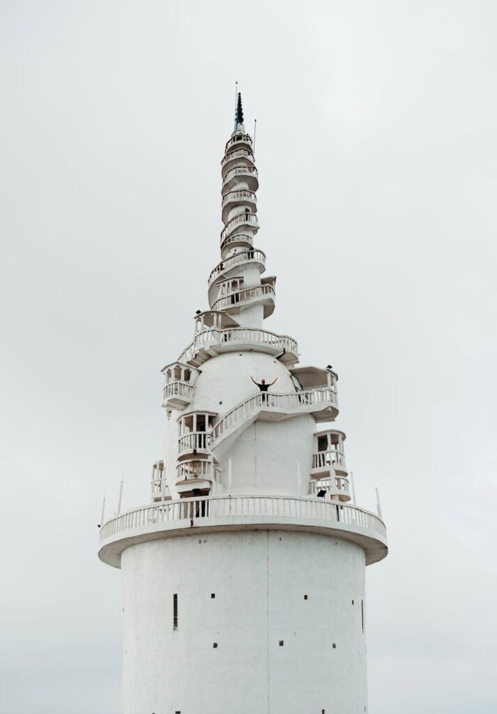 The spiraling white tower of Ambuluwawa in Sri Lanka, with Caleb standing on one of the balconies with arms in the air. This unique architectural landmark offers panoramic views.