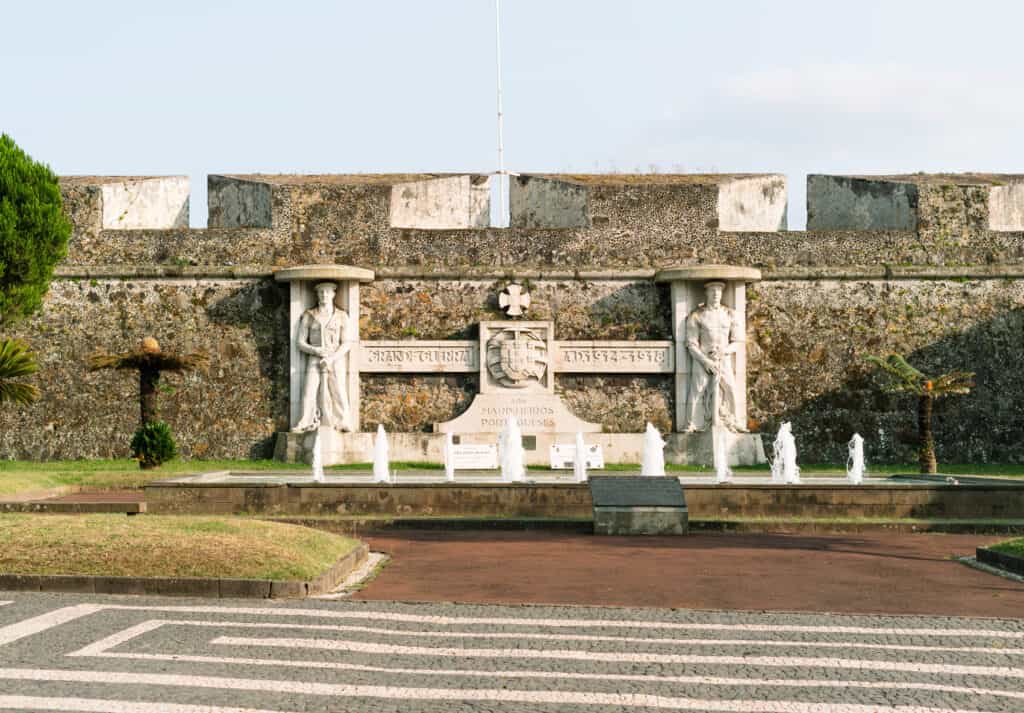 Memorial monument in Ponta Delgada dedicated to Portuguese sailors, featuring two statues of soldiers flanking an inscription and crest. The monument is set against a stone wall with a small fountain in front, commemorating those who served during World War I.