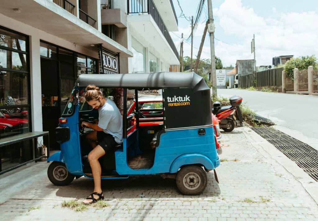 caleb climbing into our blue tuk-tuk after renting a Tuktuk in Sri Lanka. The tuk-tuk sits 4 people and is from tuktukrental.com
