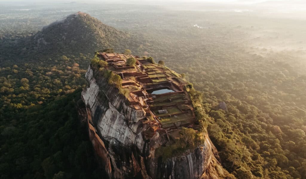 Aerial view of the Sigiriya Rock Fortress in Sri Lanka, highlighting the ancient ruins and terraced gardens at the summit of the massive rock.