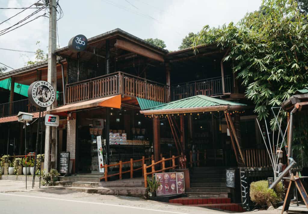Street view of a rustic café and tea shop in Ella, Sri Lanka, '360 Ella.' The storefront displays tea products, a small chalkboard menu, and outdoor seating.